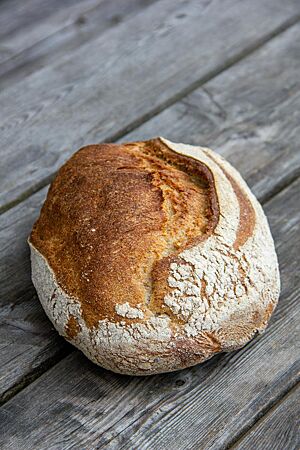 Rustikales Weizenmischbrot. Ein kräftig ausgebackenes Weizenmischbrot liegt auf einem rustikalen Holztisch.