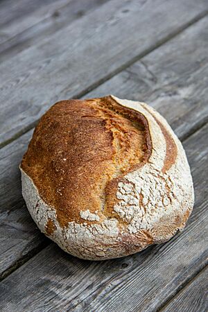 Ein kräftig ausgebackenes Weizenmischbrot liegt auf einem rustikalen Holztisch.