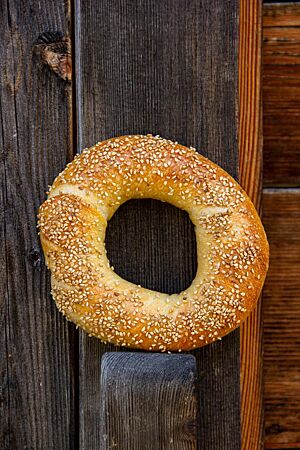 Sauerteigbagel. Ein goldgelb ausgebackener Bagel mit Sesam auf der Kruste lehnt an einer Holzwand.