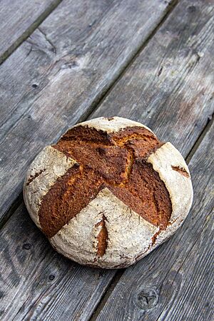 Ein kräftig ausgebackenes Weizenmischbrot mit bemehlter Kruste liegt auf einem rustikalen Holztisch.