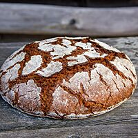 Das kräftig ausgebackene Roggenbrot mit bemehlter Kruste liegt auf einem rustikalen Holztisch.