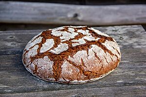 Das kräftig ausgebackene Roggenbrot mit bemehlter Kruste liegt auf einem rustikalen Holztisch.