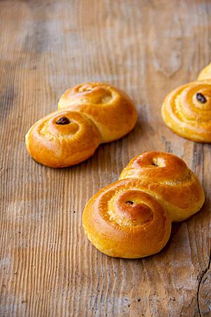 Schwedische Lussekatter. Zwei goldgelb ausgebackene Lussekatter mit glänzender Oberfläche sind als Doppelschnecke in Form einer „Acht“ gestaltet. In der Mitte jeder Schnecke liegt eine Rosine.
