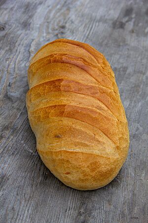 Ein goldgelb ausgebackenes, längliches Weißbrot mit gefensterter Kruste liegt auf einem rustikalen Holztisch.