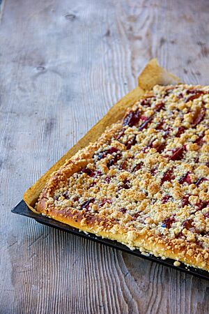 Streuselkuchen. Ein goldbraun ausgebackener Streuselkuchen liegt in einem Blech auf einem rustikalen Holztisch.