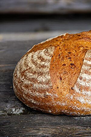 Tobias’ Kürbisruchbrot. Das kreuzweise eingeschnittene und weit aufgerissene Kürbisruchbrot liegt auf einer rustikalen Holzplatte.
