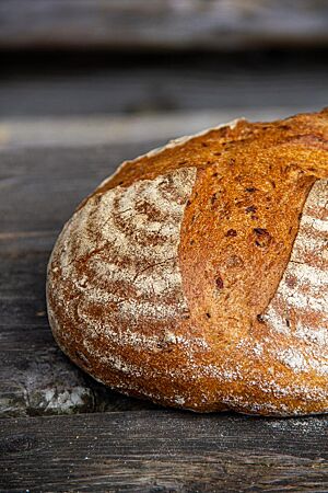 Das kreuzweise eingeschnittene und weit aufgerissene Kürbisruchbrot liegt auf einer rustikalen Holzplatte.