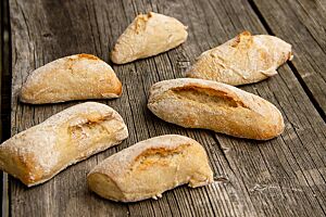 Die hell ausgebackenen, rechteckigen Brötchen mit leicht bemehlter Kruste liegen auf einem rustikalen Holztisch.