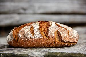 Das kräftig ausgebackene Roggenvollkornbrot mit Emmer liegt auf einem rustikalen Holztisch.