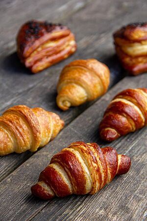 Veganer Plunderteig (Croissants). Knusprig ausgebackene Laugencroissants, Croissants und Laugenecken liegen auf einem rustikalen Holztisch.