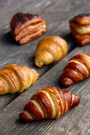 Knusprig ausgebackene Laugencroissants, Croissants und Laugenecken liegen auf einem rustikalen Holztisch.