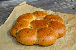 Pampuschki. Acht kleine Weizenbrötchen liegen aneinandergebacken in Form einer Blüte auf Backpapier.