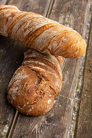 Ein kräftig ausgebackenes Wurzelbrote ohne Walnüsse liegt über einem Wurzelbrot mit Walnüssen auf einem rustikalen Holztisch.