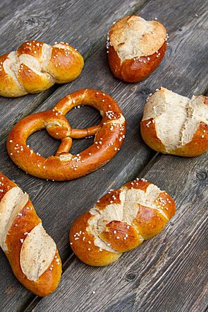 Laugengebäck in Form von Brezeln, Zöpfen, Stangen und Brötchen liegt auf einem rustikalen Holztisch..