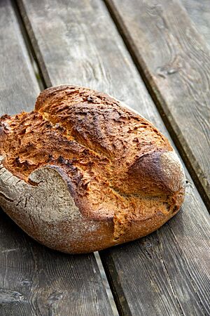 Vierkornbrot. Das kräftig ausgebackene, rustikal aufgerissene Vierkornbrot liegt auf einem Holztisch.