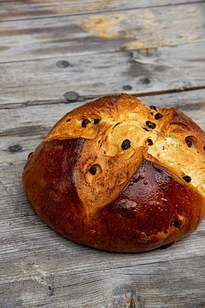 Rosinenbrot. Das dunkelbraun ausgebackene Rosinenbrot mit kreuzförmigem Einschnitt auf der Oberseite liegt auf einem rustikalen Holztisch.