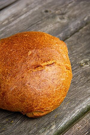 Das goldbraun ausgebackene Weizenmischbrot mit glatter, glänzender Kruste liegt auf einem rustikalen Holztisch.