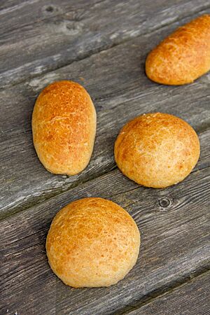 Runde und oval geformte Sandwichbrötchen mit glatter Oberfläche liegen auf einem rustikalen Holztisch.