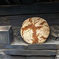Ein großer Brotlaib mit bemehlter Kruste lehnt an einer dunklen Wand.