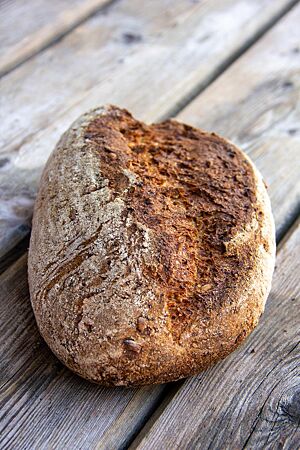 Ein kräftig ausgebackener Brotlaib liegt auf einem rustikalen Holztisch.