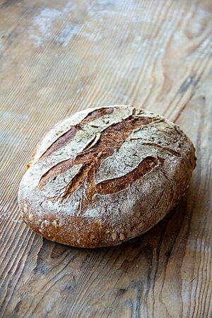 Die helle Variante des Weizenmischbrotes liegt kräftig ausgebacken auf einem Holztisch.