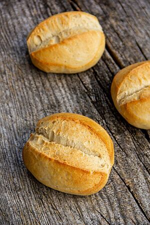 Drei ovale Brötchen mit mittig eingeschnittener Kruste liegen auf einem rustikalen Holztisch.