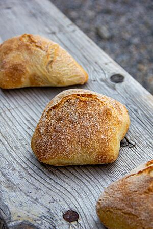 Drei kräftig ausgebackene, eckige Weizenbrötchen liegen auf einem rustikalen Holztisch.