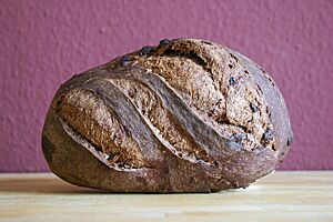 Pane al Cioccolato – Italienisches Schokoladenbrot. Das kräftig ausgebackene, rustikal aufgerissene Pane al Cioccolato liegt seitlich auf einem Holztisch.