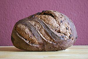 Das kräftig ausgebackene, rustikal aufgerissene Pane al Cioccolato liegt seitlich auf einem Holztisch.