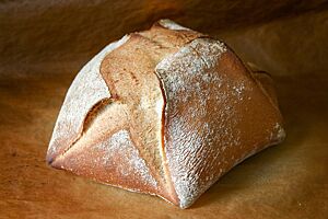 Das hellbraun ausgebackene Sechsecksbrot mit leicht bemehlter Kruste liegt auf einem Holztisch.