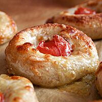 Fünf ausgebackene Kartoffel-Pizza-Nester, belegt mit Mozzarella und einer kleinen Tomate, liegen auf Backpapier.
