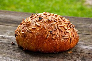 Estnisches Gelbbrot (Kollani sai). Das mit Mandelstiften bestreute, goldbraun ausgebackene Weizenbrot liegt auf einem rustikalen Holztisch.