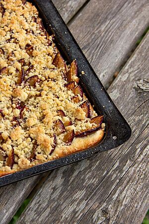 Der ausgebackene Sauerteig-Blechkuchen ist mit Pflaumen und Streuseln belegt.