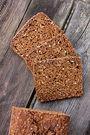 Schwarzbrot nach einer Brotbackmischung der Streichmühle: mit vielen Saaten. Im angeschnittenen Schwarzbrot sind jede Menge Saaten, grober Roggenschrot und Buchweizenkörner in der dunkelbraunen Krume zu sehen.