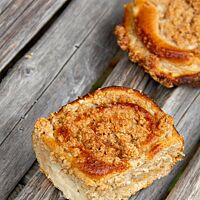 Zwei goldbraun ausgebackene Vollkornpuddingschnecken liegen auf einem rustikalen Holztisch.