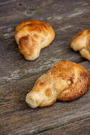 Die goldgelb bis goldbraun ausgebackenen Dinkelknauzenwecken mit ihrem typischen spitz zulaufenden Austrieb liegen auf einem rustikalen Holztisch.