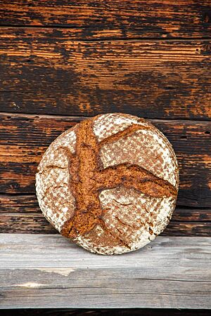 Roggenvollkornbrot mit Spezialquellstück. Das kräftig ausgebackene, rustikal aufgerissene Roggenvollkornbrot lehnt an einer Holzwand.