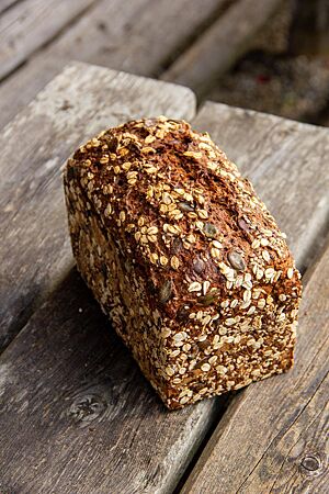 Saftkornbrot (nach einem Brot der Bäckerei „Zeit für Brot“). Das kräftig ausgebackene Saftkornbrot in Form eines Kastenbrotes liegt auf einem rustikalen Holztisch.