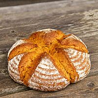 Das runde Kürbisbrot mit bemehlter Kruste liegt auf einem rustikalen Holztisch.