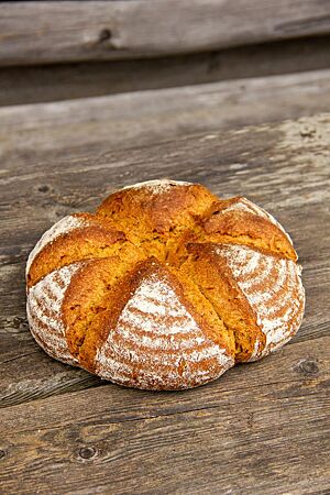 Das runde Kürbisbrot mit bemehlter Kruste liegt auf einem rustikalen Holztisch.