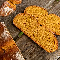 Im Anschnitt zeigt das Kürbisbrot die orangefarbene Krume umgeben von der braunen Kruste.