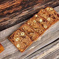 Sechs Scheiben des Haselnuss-Pflaumen-Brotes liegen aneinandergereiht auf einer rustikalen Holzbank.