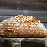 Das kräftig ausgebackene Weizen-Roggen-Mischbrot mit leicht bemehlter Kruste liegt auf einem Holztisch.