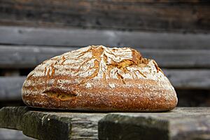 Das kräftig ausgebackene Weizen-Roggen-Mischbrot mit leicht bemehlter Kruste liegt auf einem Holztisch.