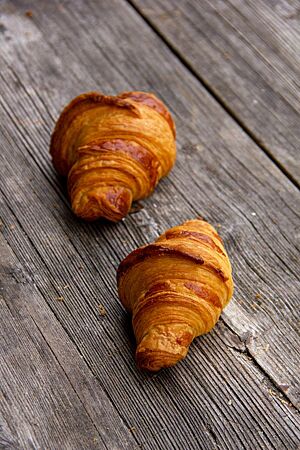 Dinkelcroissants (2021). Zwei goldgelb ausgebackene Dinkelcroissants mit glänzender Oberfläche liegen auf einem rustikalen Holztisch.