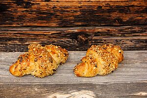 Zwei hellbraun ausgebackene Croissants mit einer Saatenmischung auf der Kruste liegen auf einem rustikalen Holztisch.