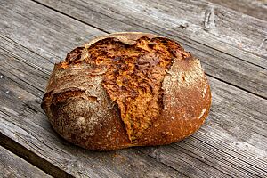König-Thomas-Brot. Das kräftig ausgebackene, rustikal aufgerissene König-Thomas-Brot liegt auf einem Holztisch.