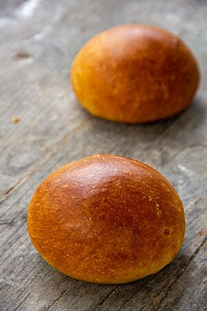 Zwei goldbraun ausgebackene Brioche-Buns mit glatter Oberfläche liegen auf einem rustikalen Holztisch.