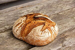 Das kräftig ausgebackene, runde Schwarzgerstebrot liegt auf einem rustikalen Holztisch.