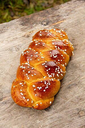 Der goldbraun ausgebackene Faserzopf mit Hagelzucker auf der Kruste liegt auf einem Holztisch.